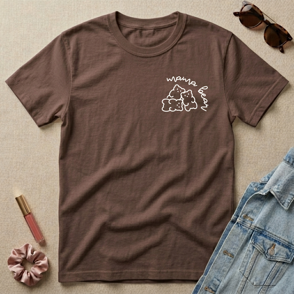 Brown t-shirt with 'mama bear' graphic on a beige surface with sunglasses, scrunchie, and lip gloss.